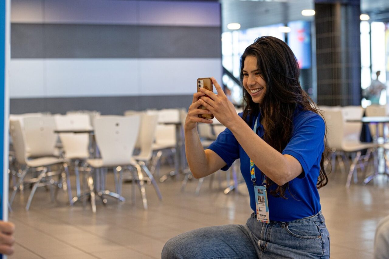 A smiling volunteer in a blue polo takes a photo with her phone at EPC 2023.